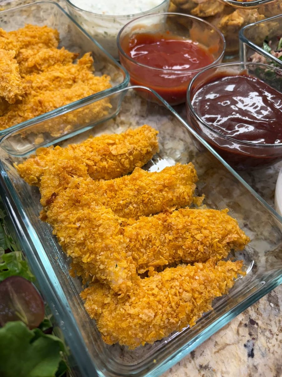 Craggy golden crust shatters over baked chicken tenders; sweet chili ketchup and raspberry reduction wait beside.