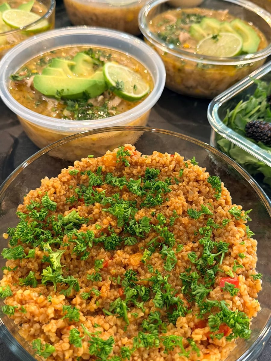 Turkish bulgur pilaf mounds in a glass bowl, red pepper through the grain, curly parsley on top.
