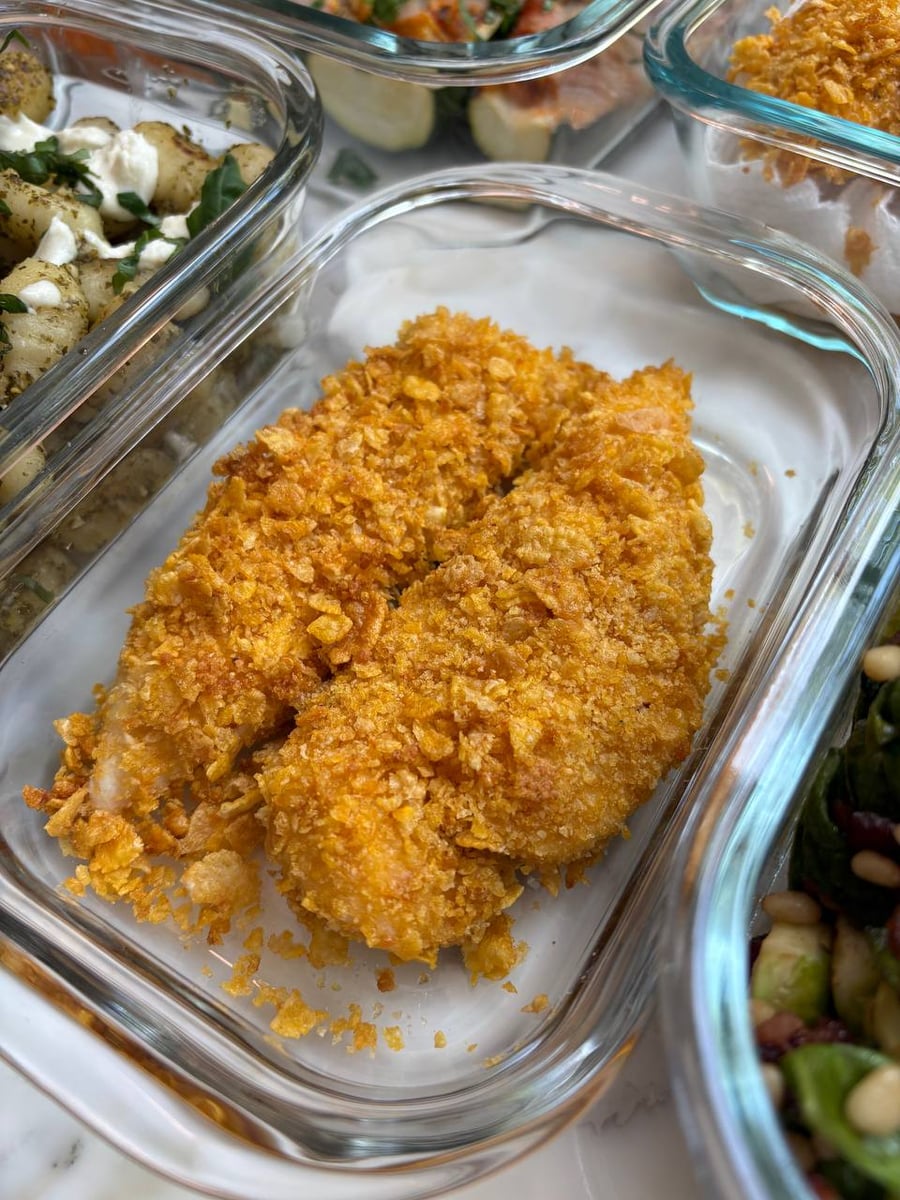 Crushed cornflakes bake into a deep orange shell over two chicken tenders, pesto gnocchi behind them.