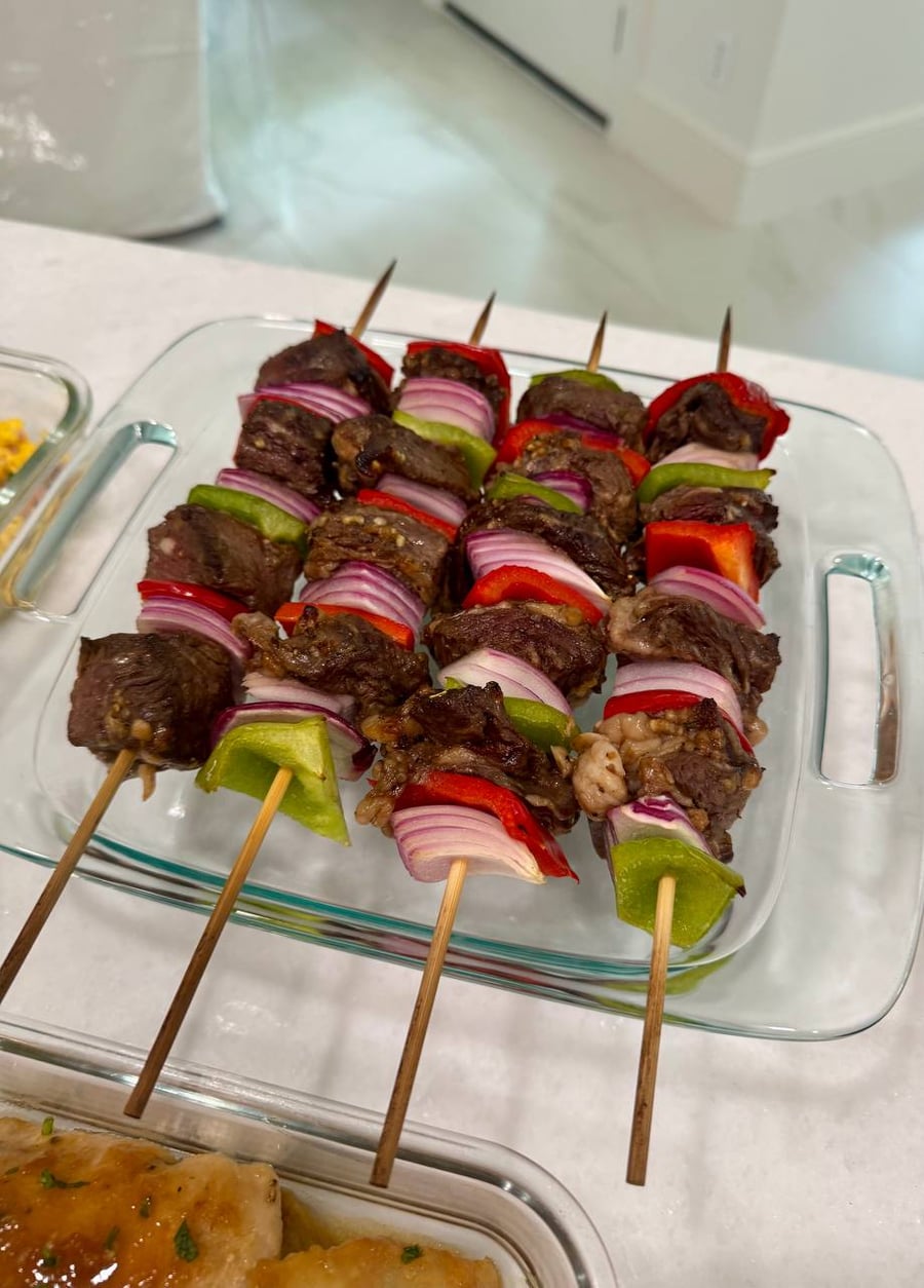 Bell peppers alternate with red onion along four beef sirloin skewers in their glass tray.