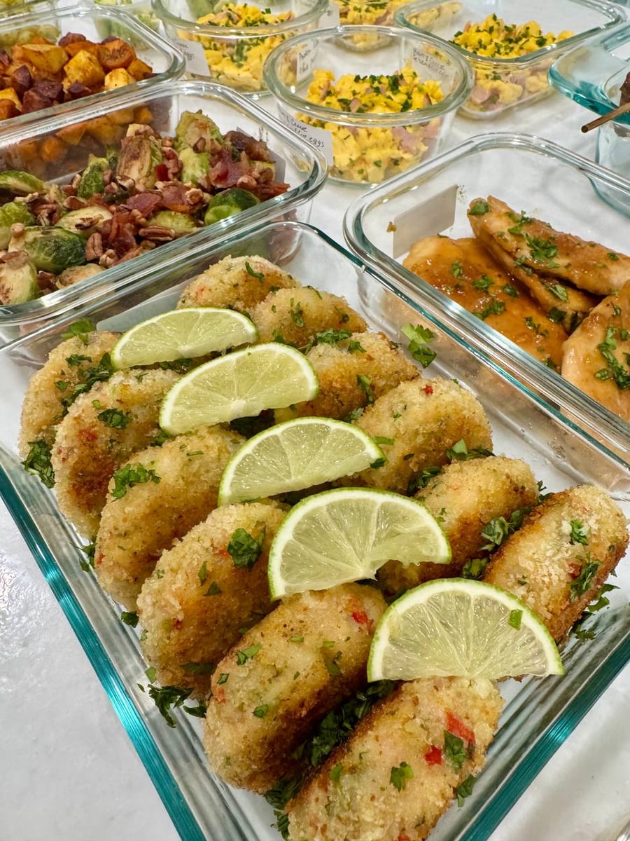 Lime wheels lean against the panko shrimp cakes, bacon brussel sprouts and sweet potatoes behind them.