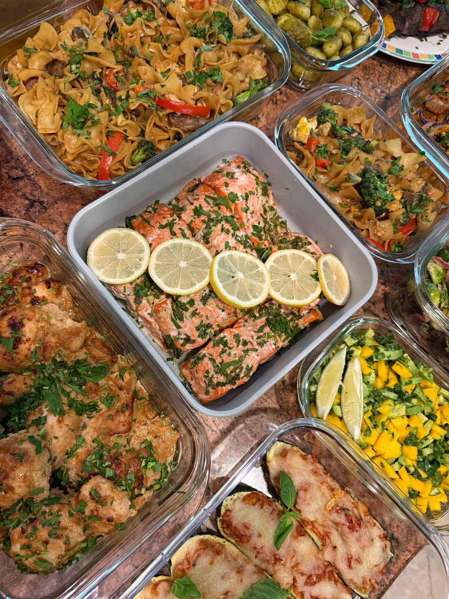 Chopped herbs cover the honey garlic salmon under a row of lemon wheels, noodles filling the tray behind.