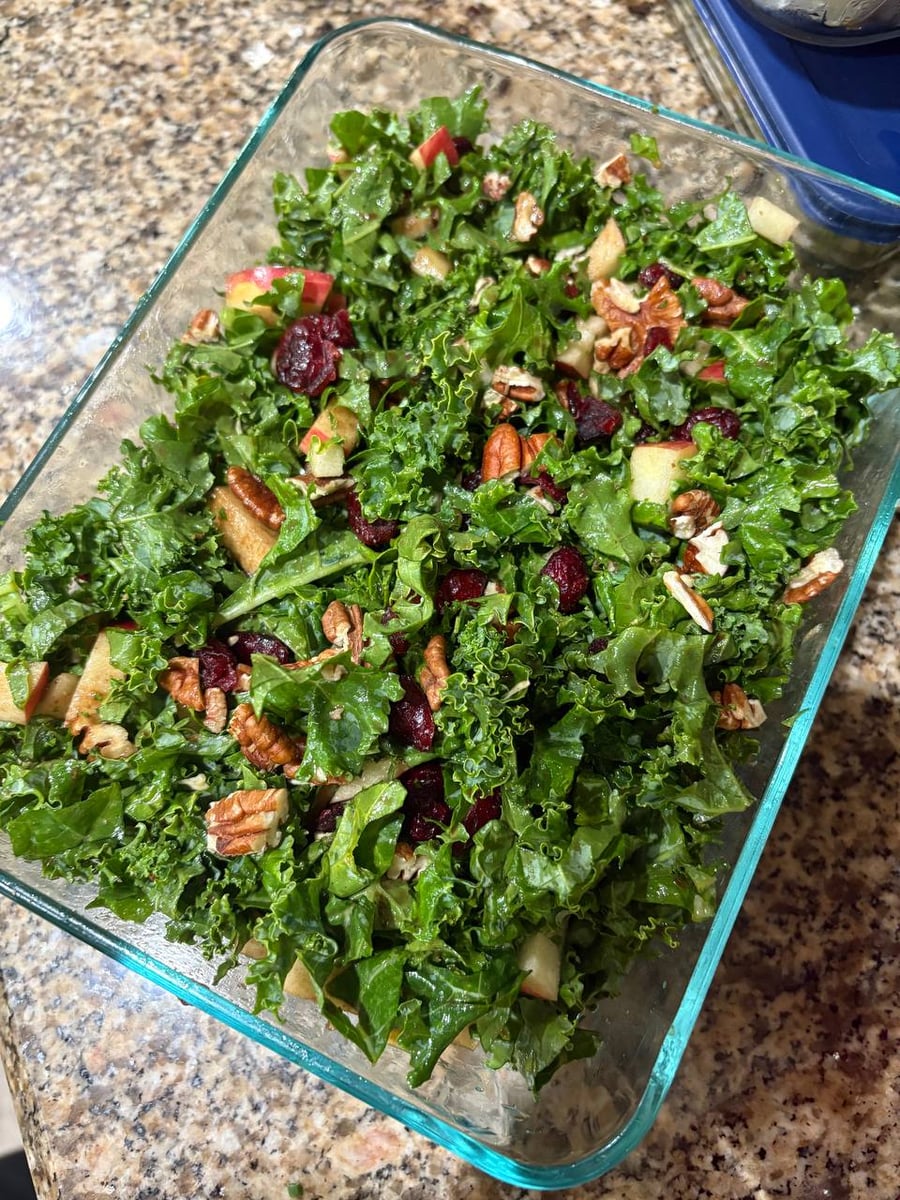 A glass container filled with a crisp kale salad tossed with sweet dried cranberries, crunchy pecans, and fresh Gala apple slices for a vibrant texture.
