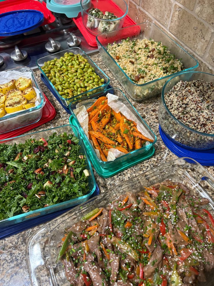 A variety of glass storage containers filled with Mongolian beef, kale apple salad, coriander roasted carrots, charred edamame, and parsley quinoa with nuts.
