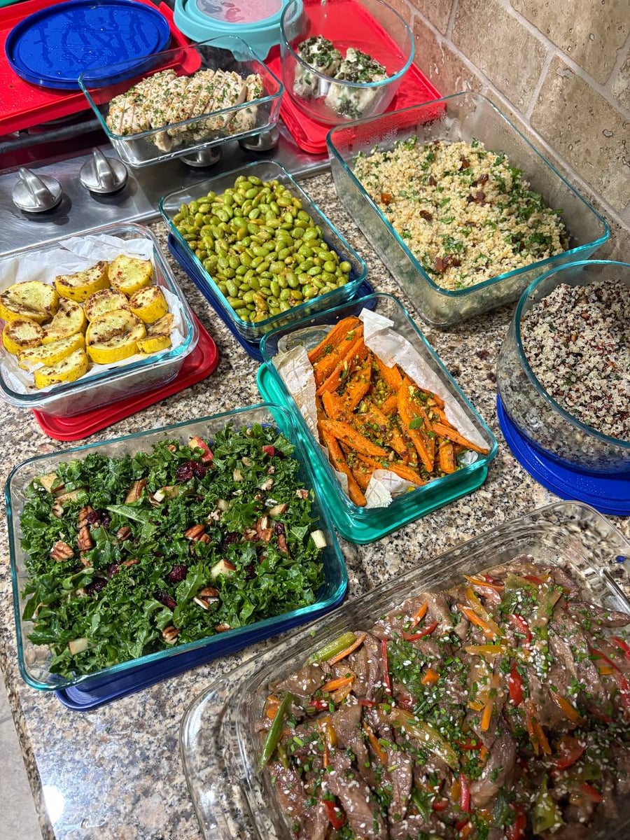 A variety of glass containers filled with items like Mongolian beef, roasted carrots, kale salad, and edamame, showcasing diverse colors and professional meal preparation.