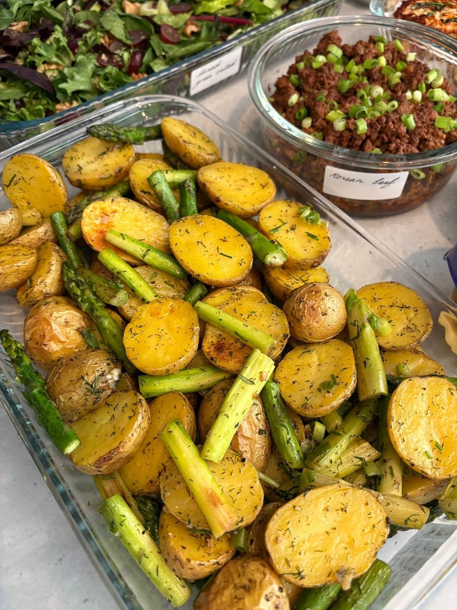 Asparagus tips lean between halved baby potatoes flecked with dill, korean beef labelled behind them.