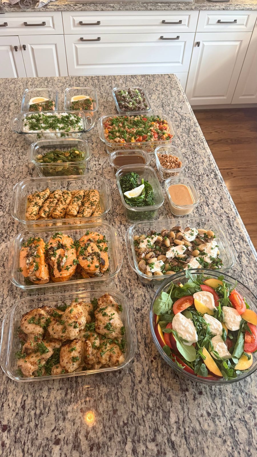 A collection of glass meal prep containers featuring Korean BBQ steak, honey lime chicken, salmon pinwheels, gnocchi, broccolini, and a fresh mozzarella peach salad.