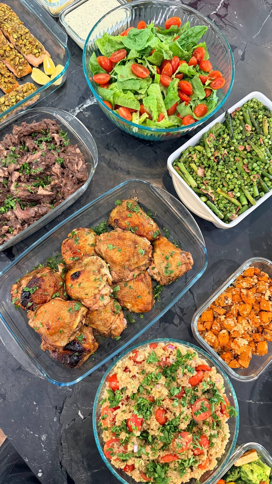 A selection of glass containers showcasing pistachio salmon, balsamic chicken, seared asparagus, quinoa salad, beef ribeye, and a fresh Caesar salad.
