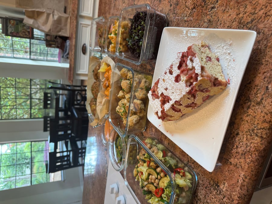An assortment of glass containers with chicken meatballs, chili broccoli, black rice, and a strawberry shortcake loaf on a white plate.