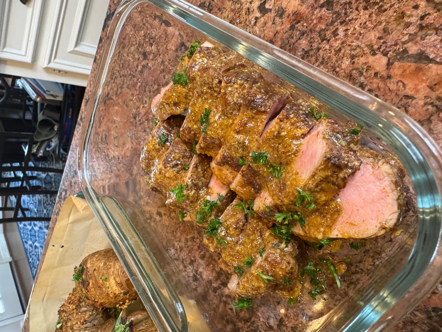 Sliced pork tenderloin coated in a rich maple mustard sauce, garnished with fresh parsley, next to a side of golden oven-roasted hasselback potatoes.
