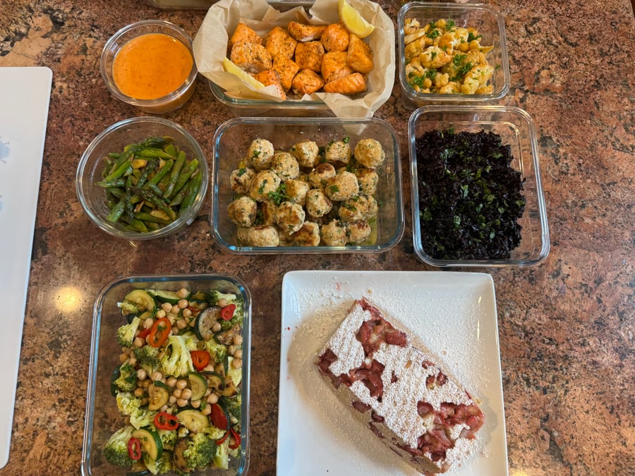 A variety of glass meal prep containers featuring garlic salmon bites, chicken picatta meatballs, cilantro black rice, ginger asparagus, vegetable stir-fry, and strawberry loaf.