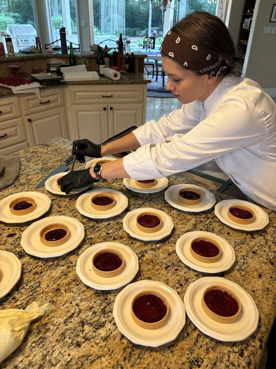 Chef Ana plating individual mini raspberry cheesecake tarts with raspberry compote in the kitchen.