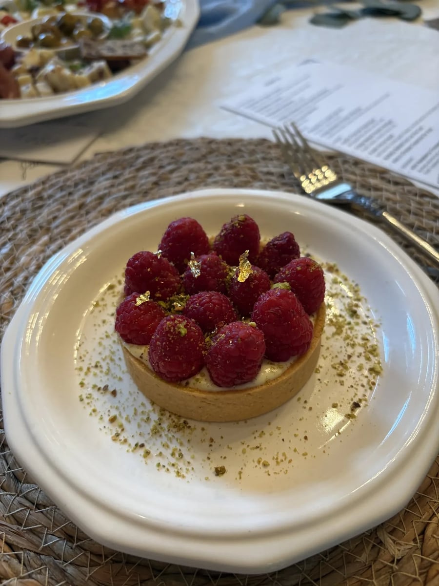 Close-up of mini raspberry cheesecake tart with gold leaf raspberries and pistachio crisps.