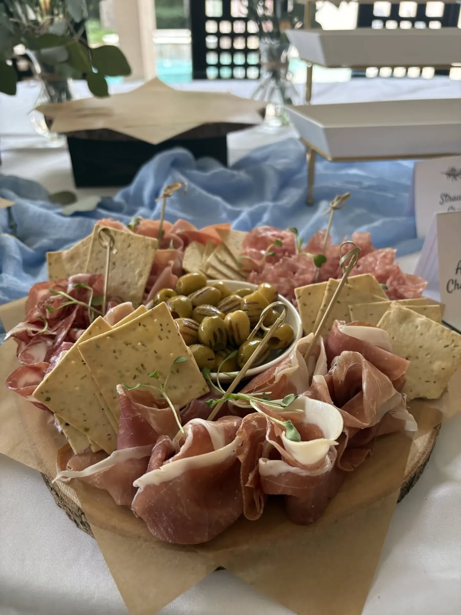 Charcuterie board with prosciutto, salami, and marinated olives on a round wooden board.
