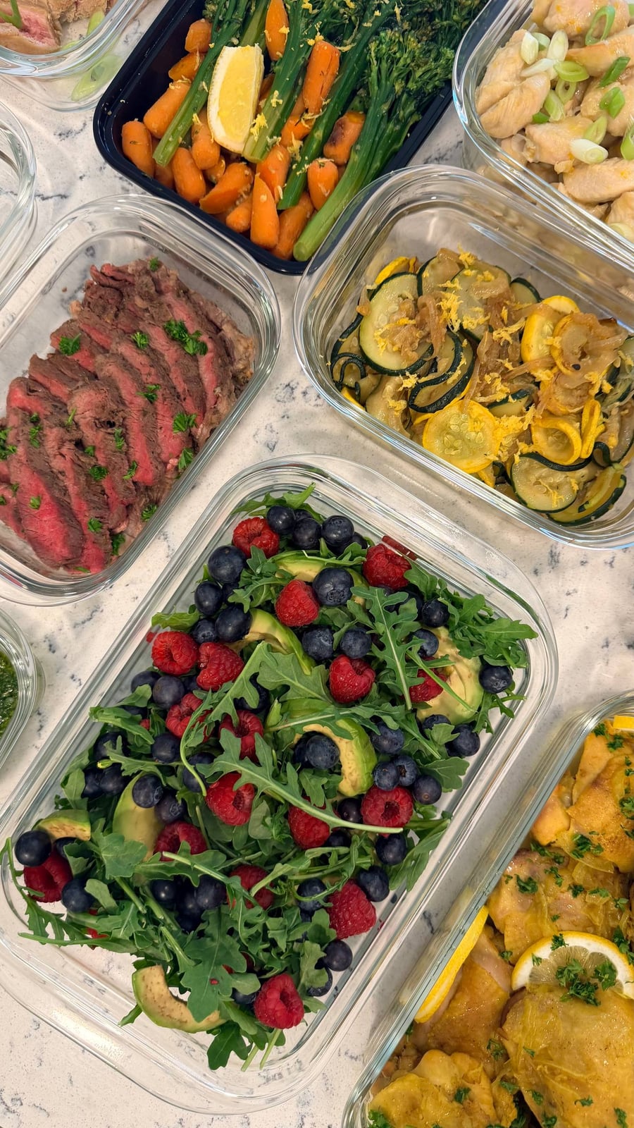 Raspberries and blueberries scatter through arugula with thick avocado slices in a clear dish.