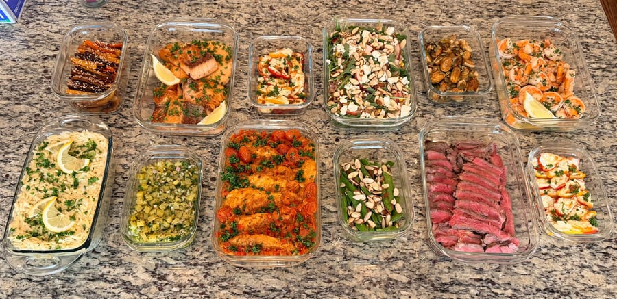 Twelve containers in two long rows, honey garlic salmon at one end and sliced strip steak at the other.
