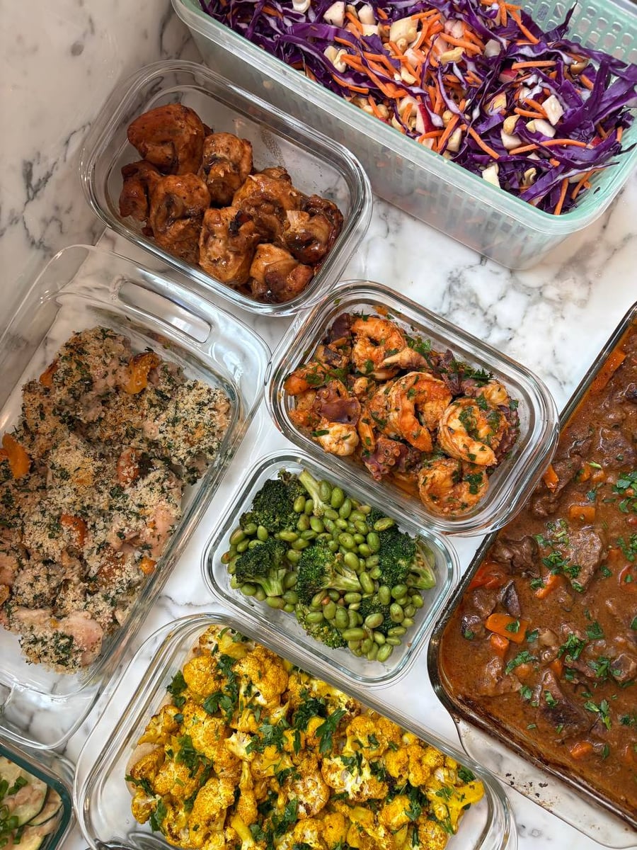 Red cabbage, carrot and cashew shreds fill a colander, apricot chicken and beef stew below it.
