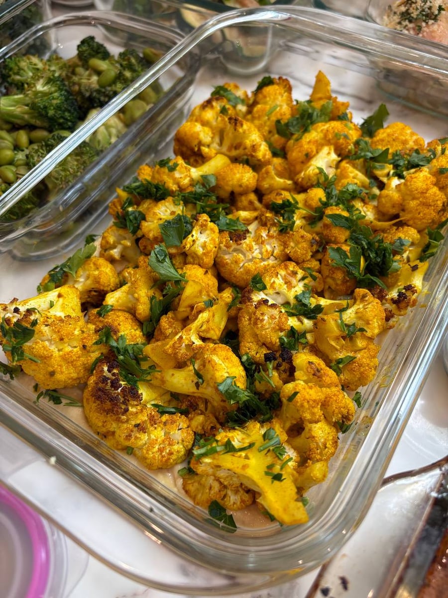 Parsley falls in handfuls over cauliflower stained deep yellow with turmeric, edges caught dark.