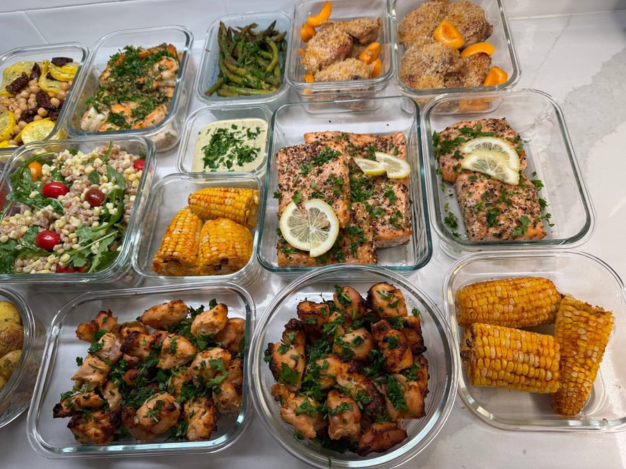 Souvlaki skewers fill two bowls at left while salmon, corn cobs and farro salad line up alongside.