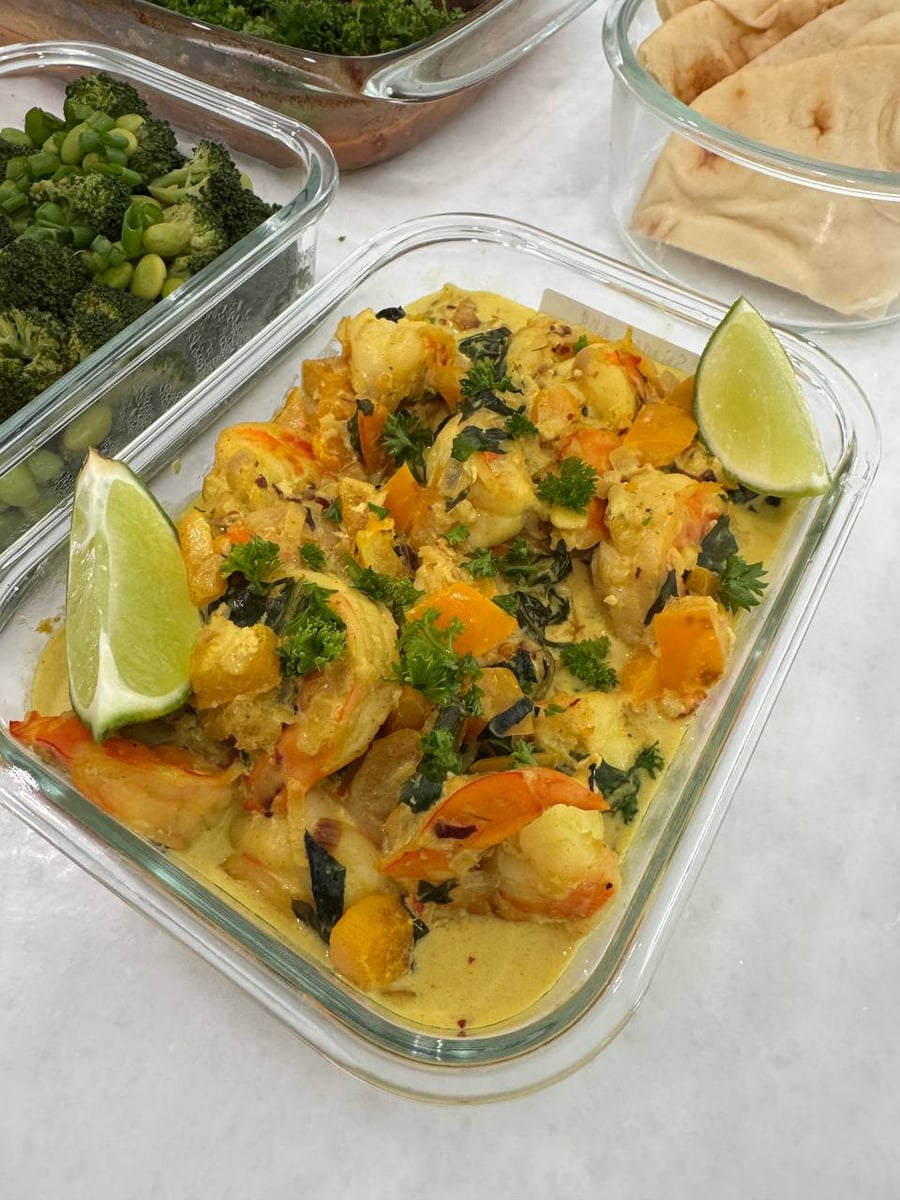 Lime wedges sit either end of shrimp in coconut sauce with squash cubes and torn spinach.