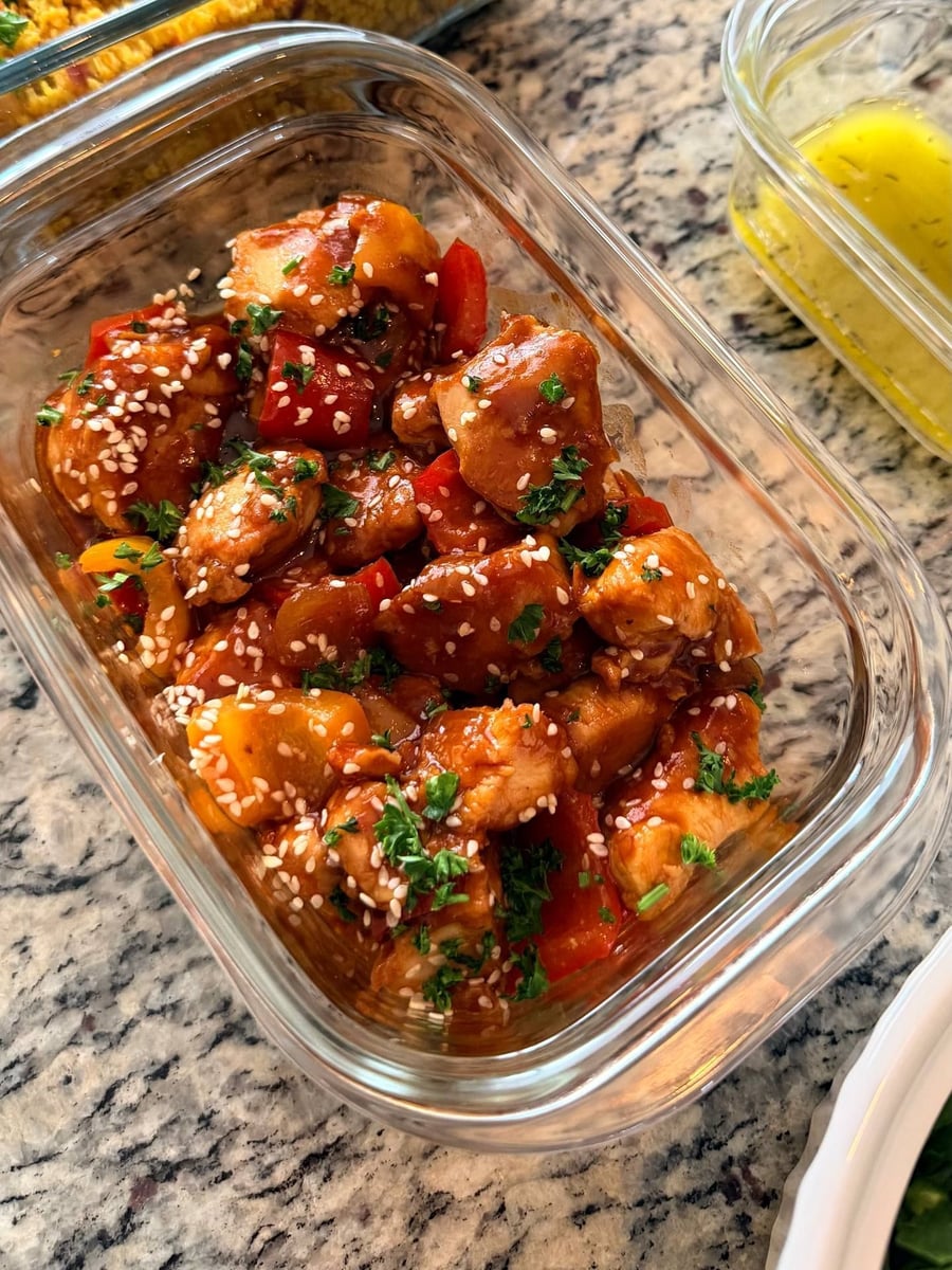 Sweet and sour chicken bites glossed red, studded with sesame seeds and cut red and yellow pepper.