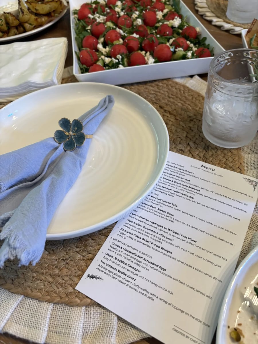 Table place setting with a periwinkle napkin and floral ring beside the Summer Weekend Brunch menu card.