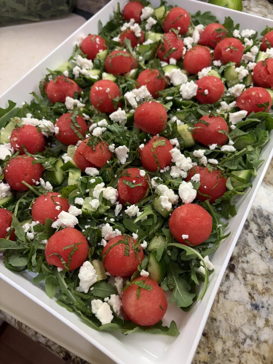Watermelon, cucumber and mint salad with arugula and crumbled honey goat cheese in a white tray.