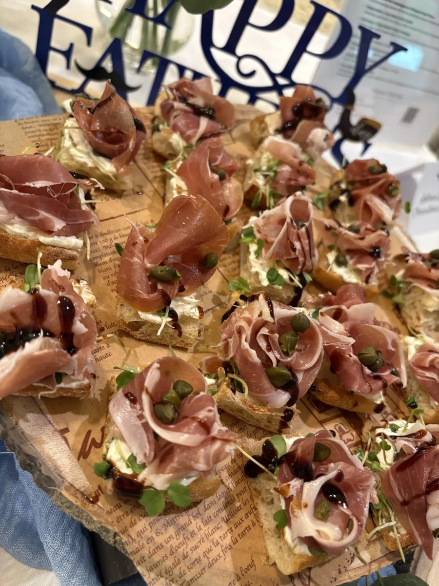Prosciutto and arugula crostini with herbed cream cheese and microgreens beside the Father's Day banner.