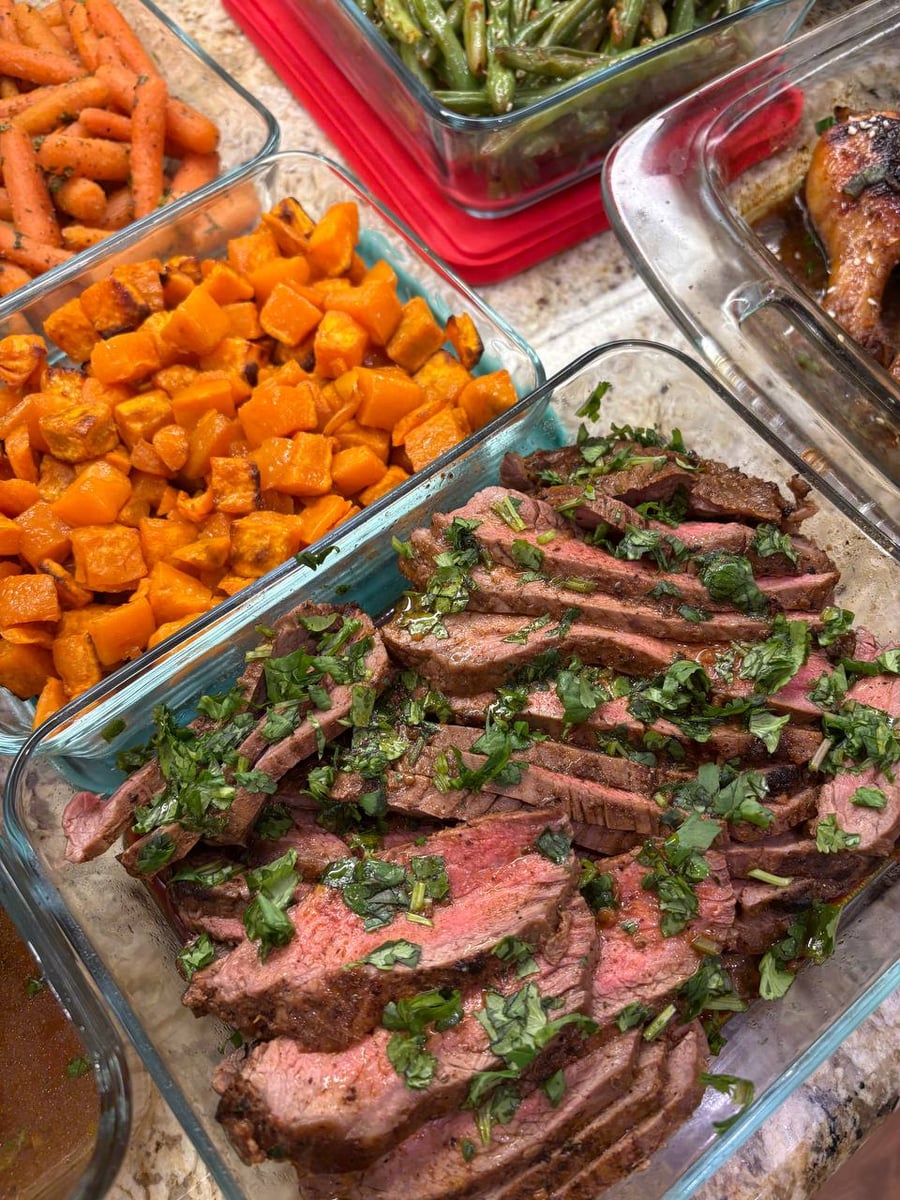 Glass containers featuring sliced, cilantro-topped carne asada flank steak beside a large portion of perfectly roasted, vibrant orange sweet potato cubes.