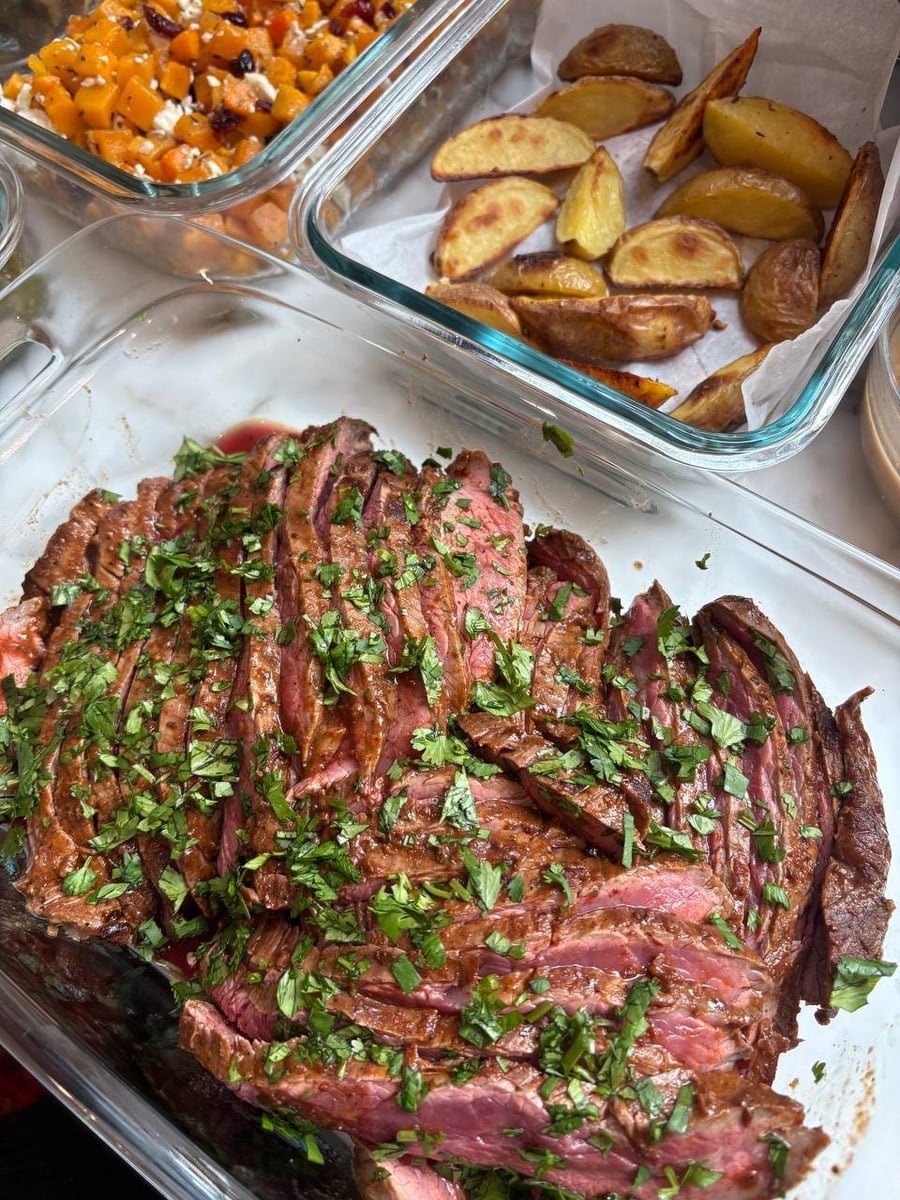 Carne asada flank steak garnished with cilantro, truffle oil potato wedges, and feta cranberry pecan butternut squash in glass meal prep containers.