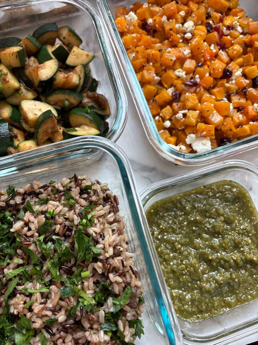 Four glass storage containers displaying seared zucchini, feta cranberry butternut squash, fresh herbed wild rice, and a vibrant green salsa verde sauce.