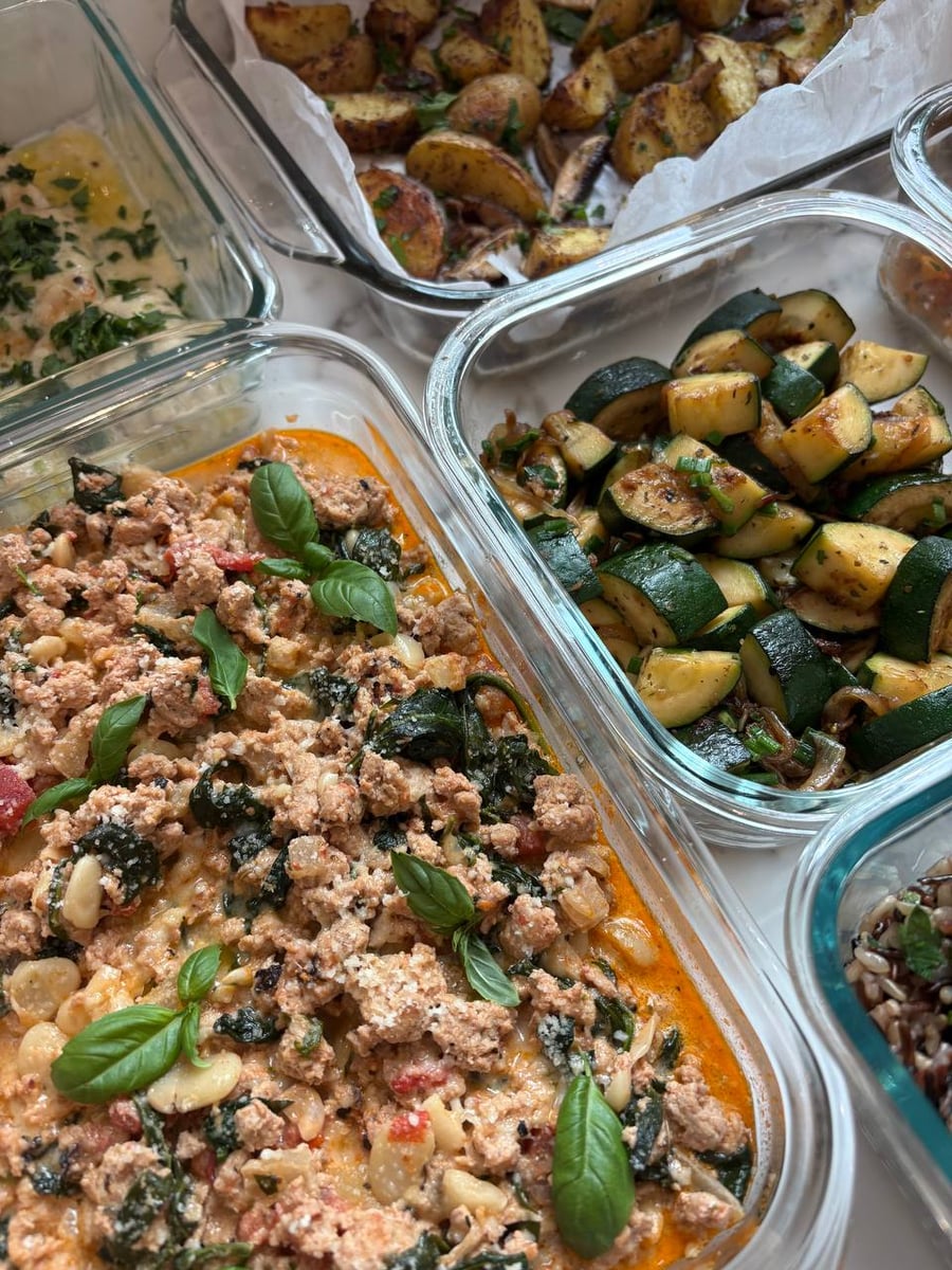 Glass containers featuring Tuscan ground turkey with spinach, seared zucchini with onions, and truffle oil baked potato wedges in a meal prep arrangement.