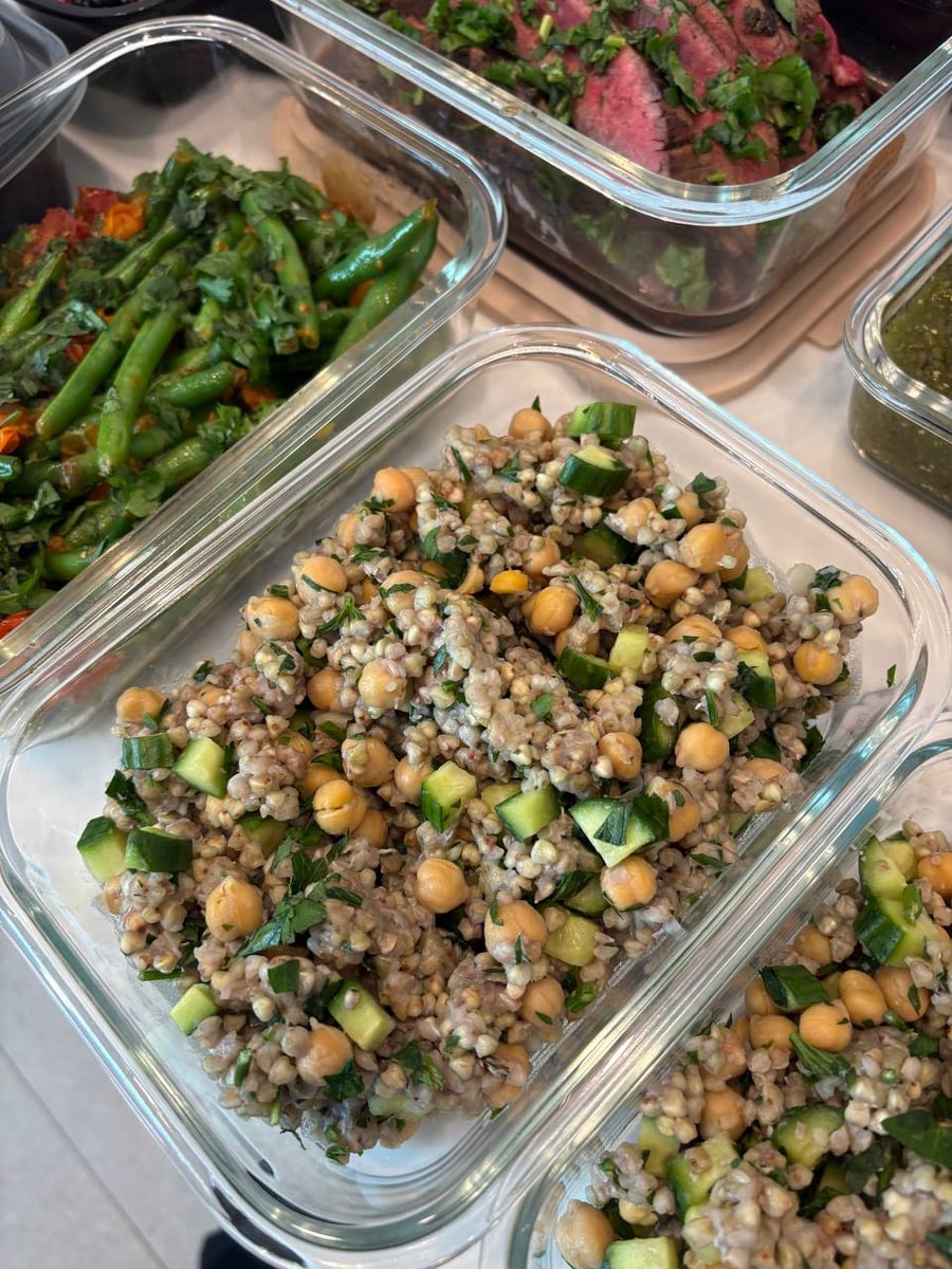 Glass meal prep containers filled with lemony green buckwheat salad featuring chickpeas, fresh cucumber cubes, and vibrant green herbs, neatly arranged on a surface.