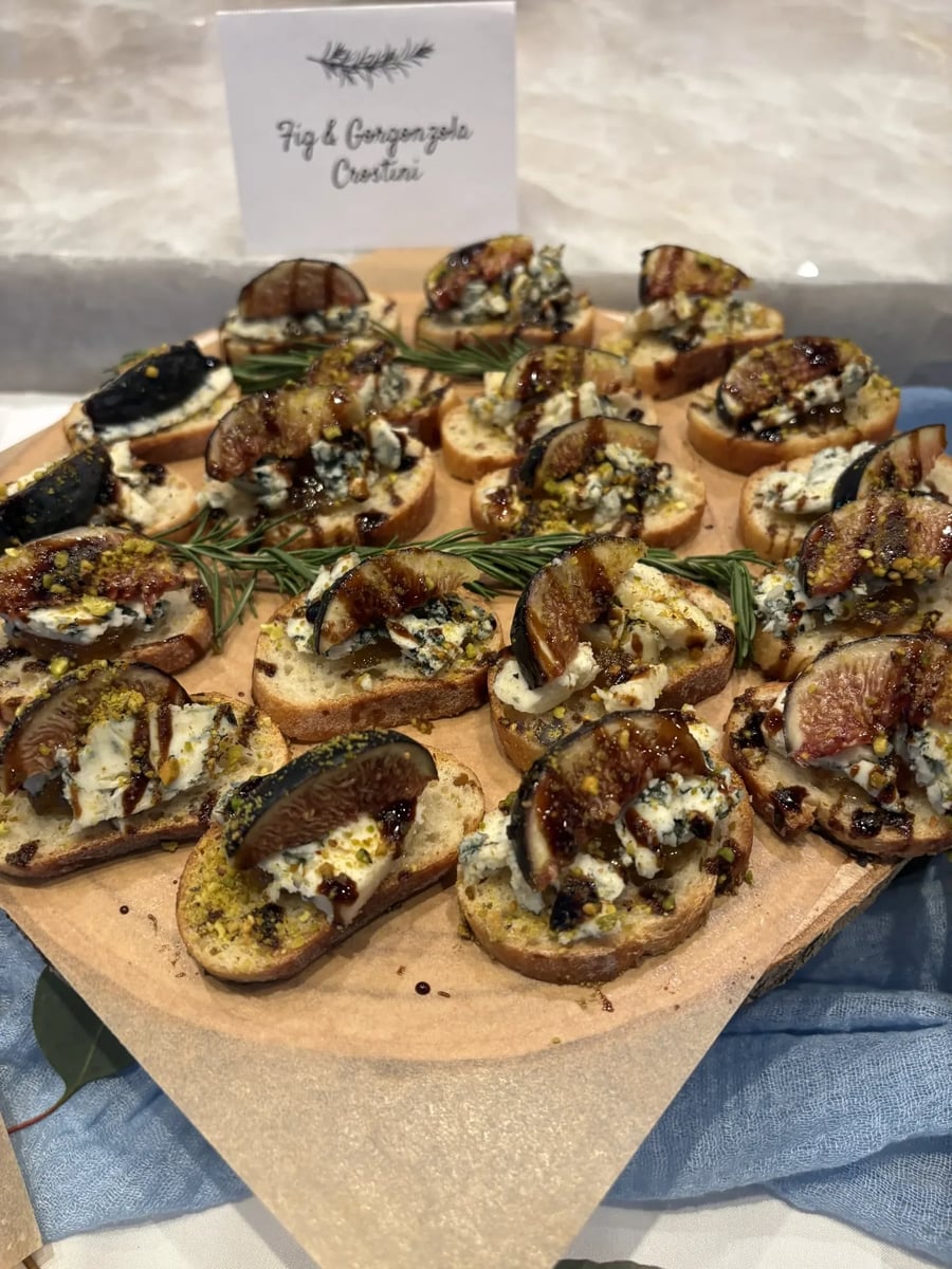 Fig and Gorgonzola crostini with candied orange jam, pistachios, and balsamic glaze — label card visible.