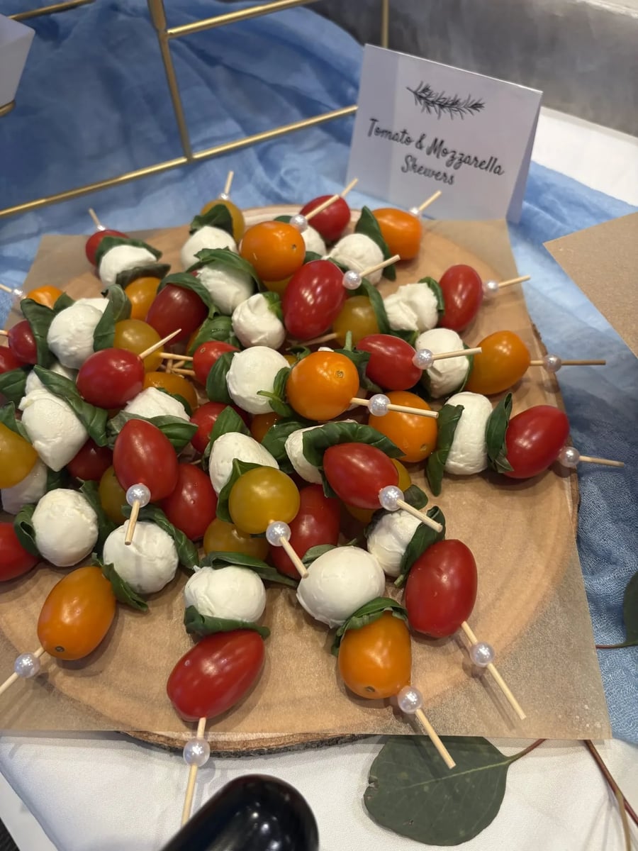 Tomato and mozzarella caprese skewers with fresh basil on a wooden board — label card visible.