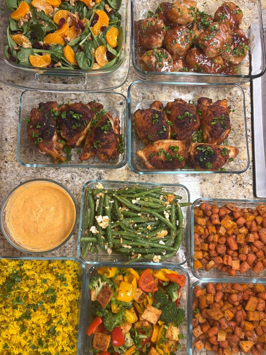 Glass containers filled with teriyaki pork, paprika chicken, saffron rice, roasted vegetables, garlic goat cheese beans, and a mandarin spinach wallnut salad.