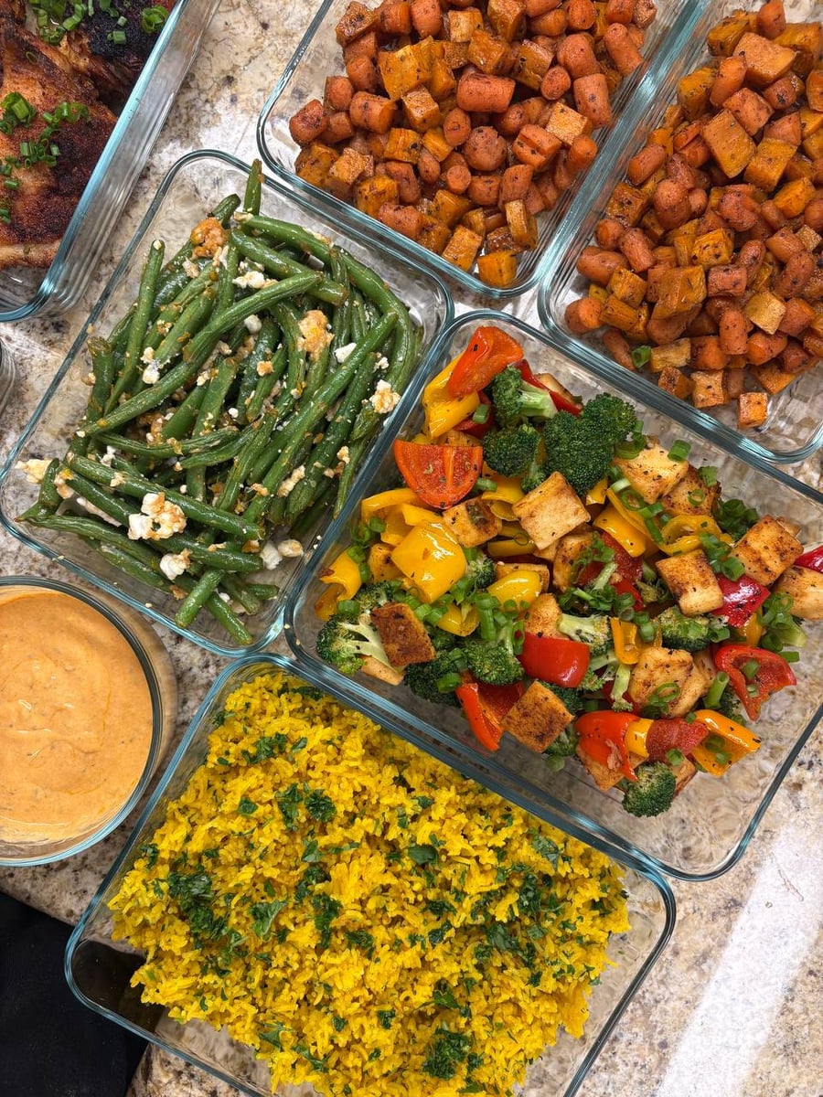 Glass containers featuring paprika chicken thighs, maple sweet potatoes, garlic goat cheese green beans, paneer stir fry, and saffron infused rice.