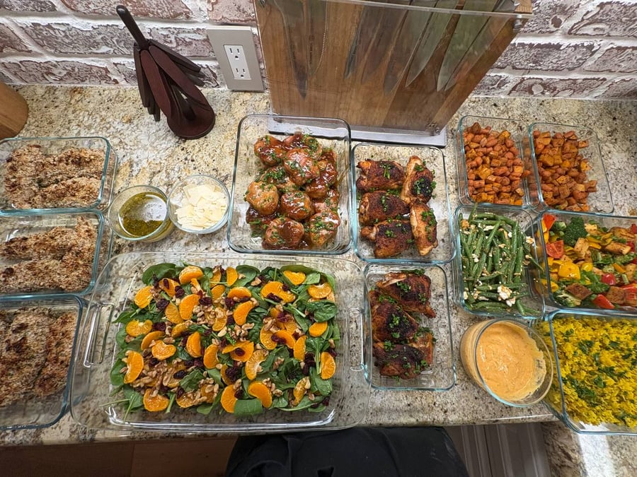 Glass containers filled with pecan-crusted chicken, teriyaki pork medallions, roasted sweet potatoes, bell pepper stir fry, spinach salad, and various savory side dishes.
