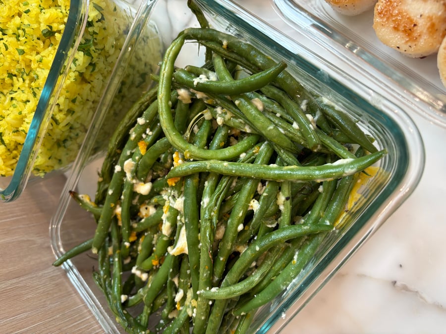 A glass storage container holding garlic and goat cheese baked French beans next to another container filled with fluffy, bright yellow saffron infused rice.