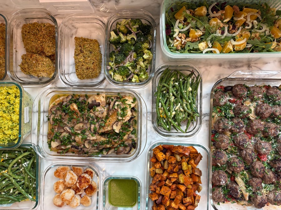 Glass containers filled with pistachio halibut, chicken marsala, garlic scallops, Greek meatballs, saffron rice, roasted vegetables, and a fresh orange fennel salad.