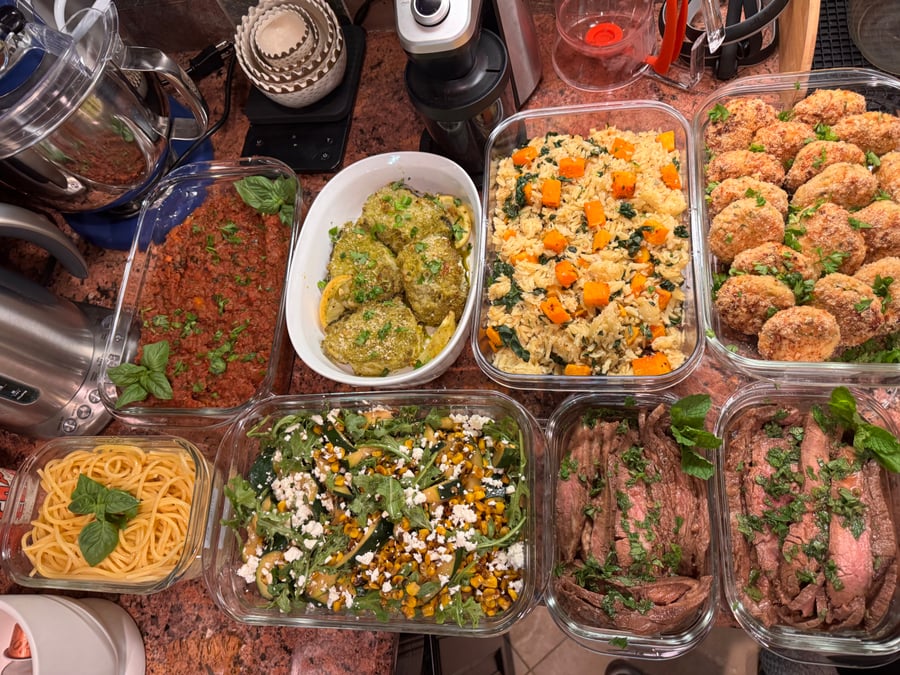 Glass containers holding Vietnamese skirt steak, mid-east chickpea salad with tomatoes and cucumbers, and honey dijon roasted cauliflower and asparagus side dishes.