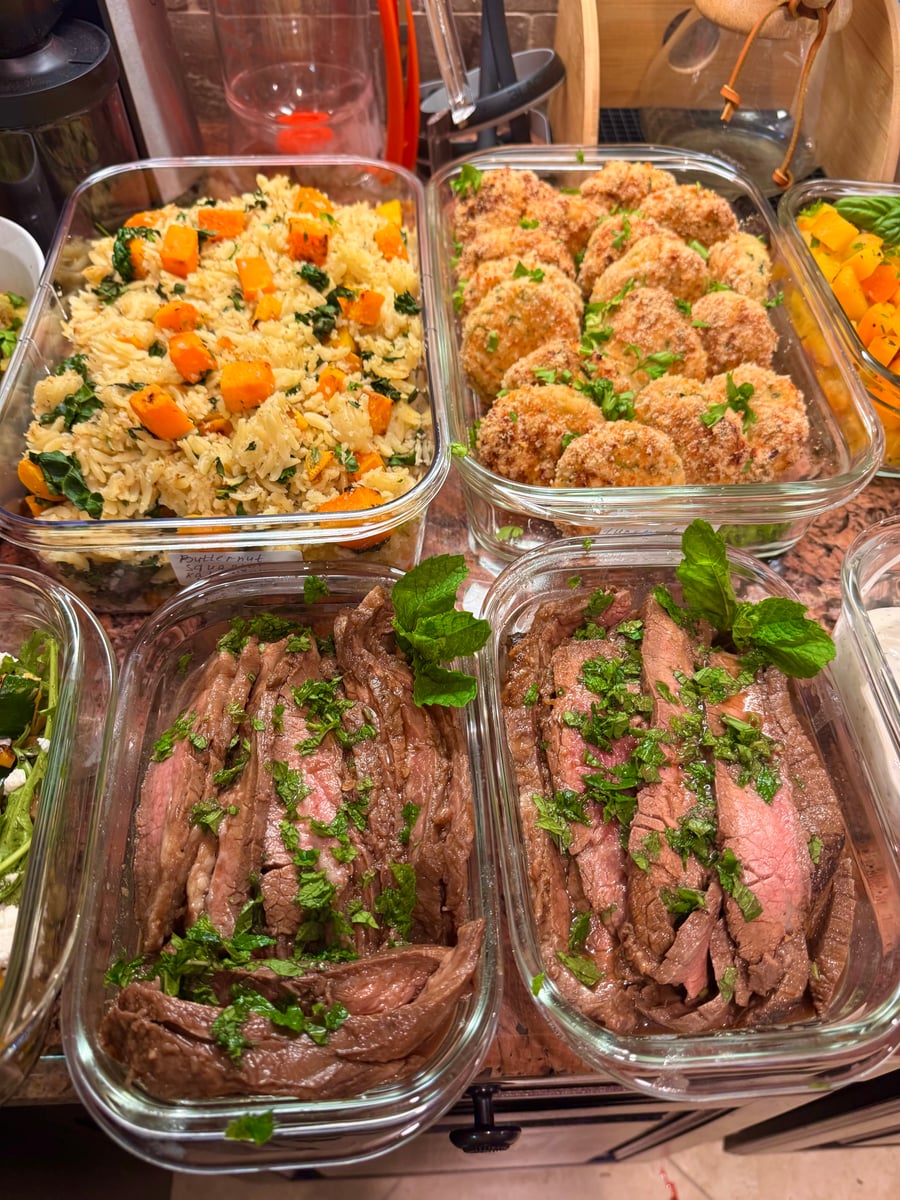 Glass meal prep containers filled with sliced flank steak with fresh herbs, golden fried savory patties, and orzo pasta with roasted butternut squash.