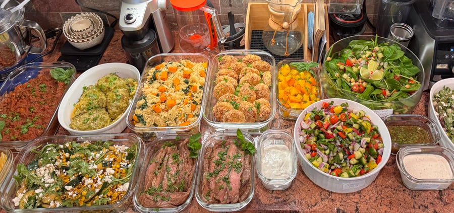 A variety of meal prep containers featuring steak slices, grain salad, breaded cutlets, fresh spinach salad, roasted vegetables, and creamy dressing dips.