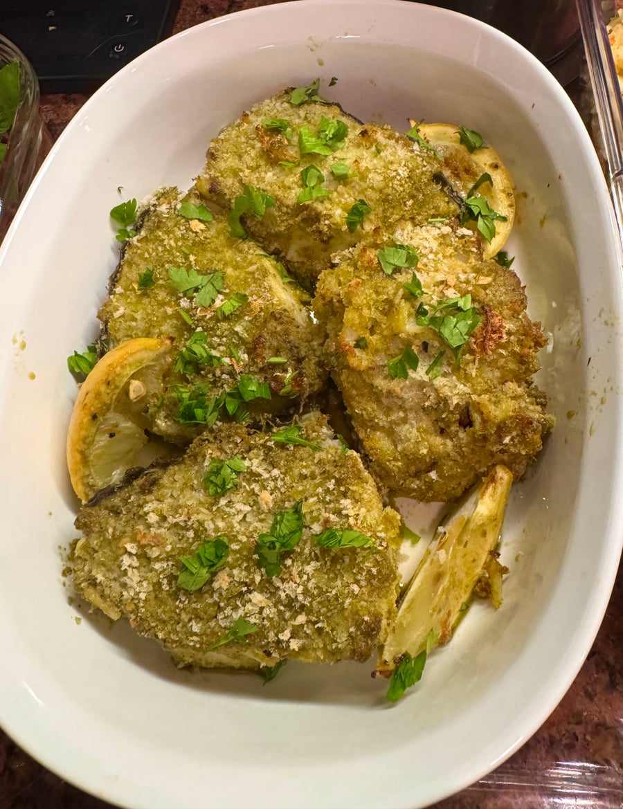This dish features delicate white fish fillets coated in a vibrant, golden-brown herb and breadcrumb crust, baked to perfection in a classic white oval dish.
