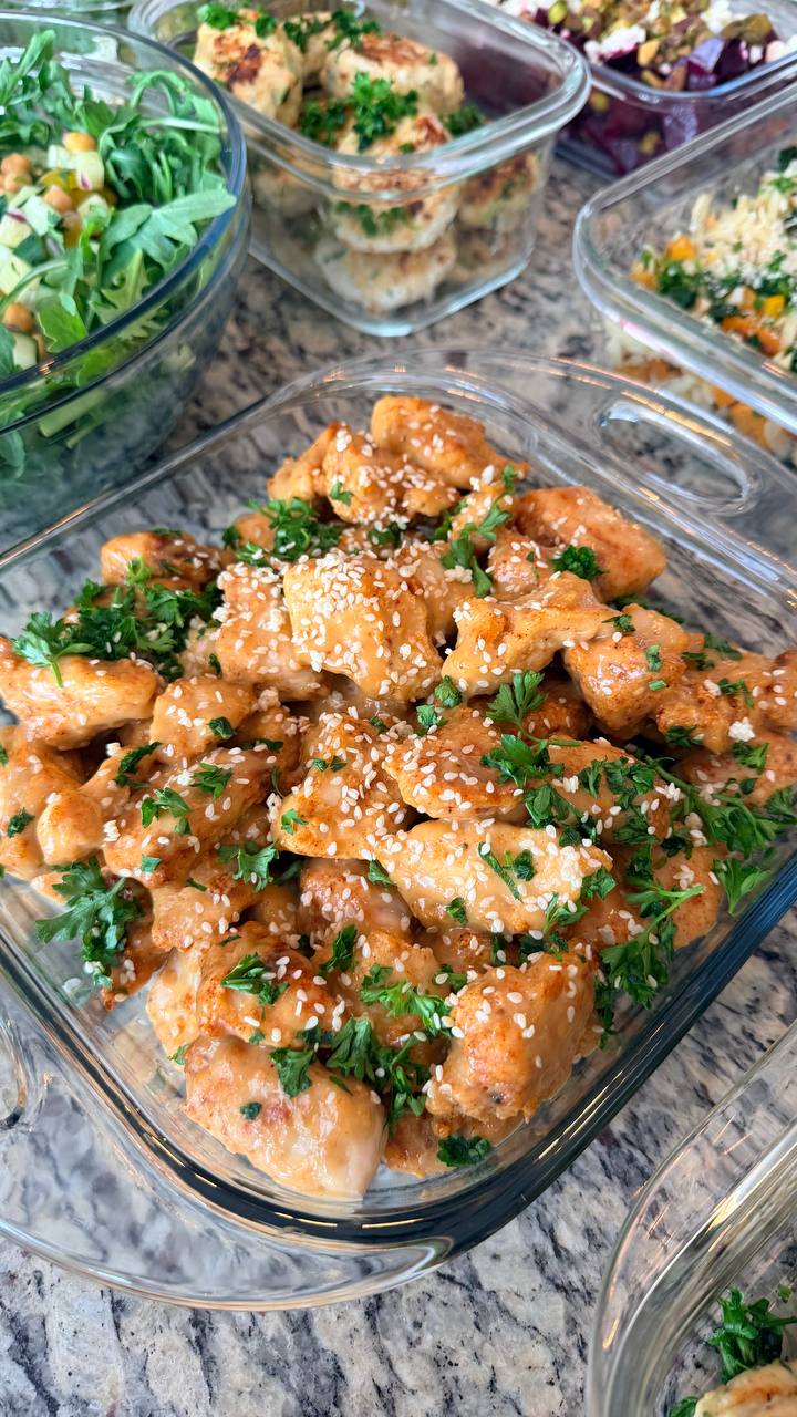 Glass meal prep containers filled with orange glazed crispy chicken bites, zucchini turkey fritters, roasted cauliflower with greens, and butternut orzo salad.