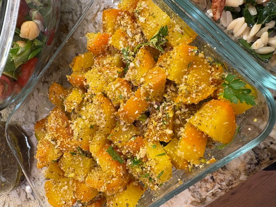A glass container filled with vibrant roasted golden beets generously coated in crunchy pistachio dukkah, fresh herbs, and aromatic toasted spices.