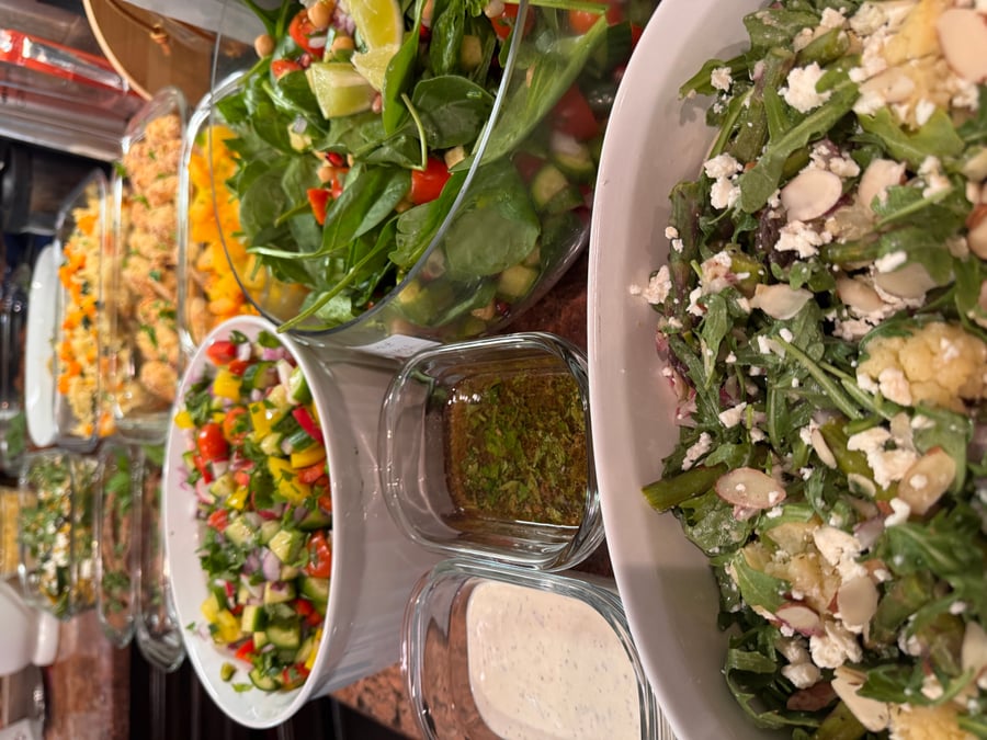 A variety of vibrant salads and dressings including roasted cauliflower, spinach salad with chickpeas, and fresh cucumber tomato salsa in serving bowls.