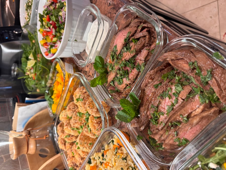 Glass meal prep containers filled with sliced medium-rare flank steak, herbed orzo, breaded zucchini coins, and a vibrant fresh vegetable salad.