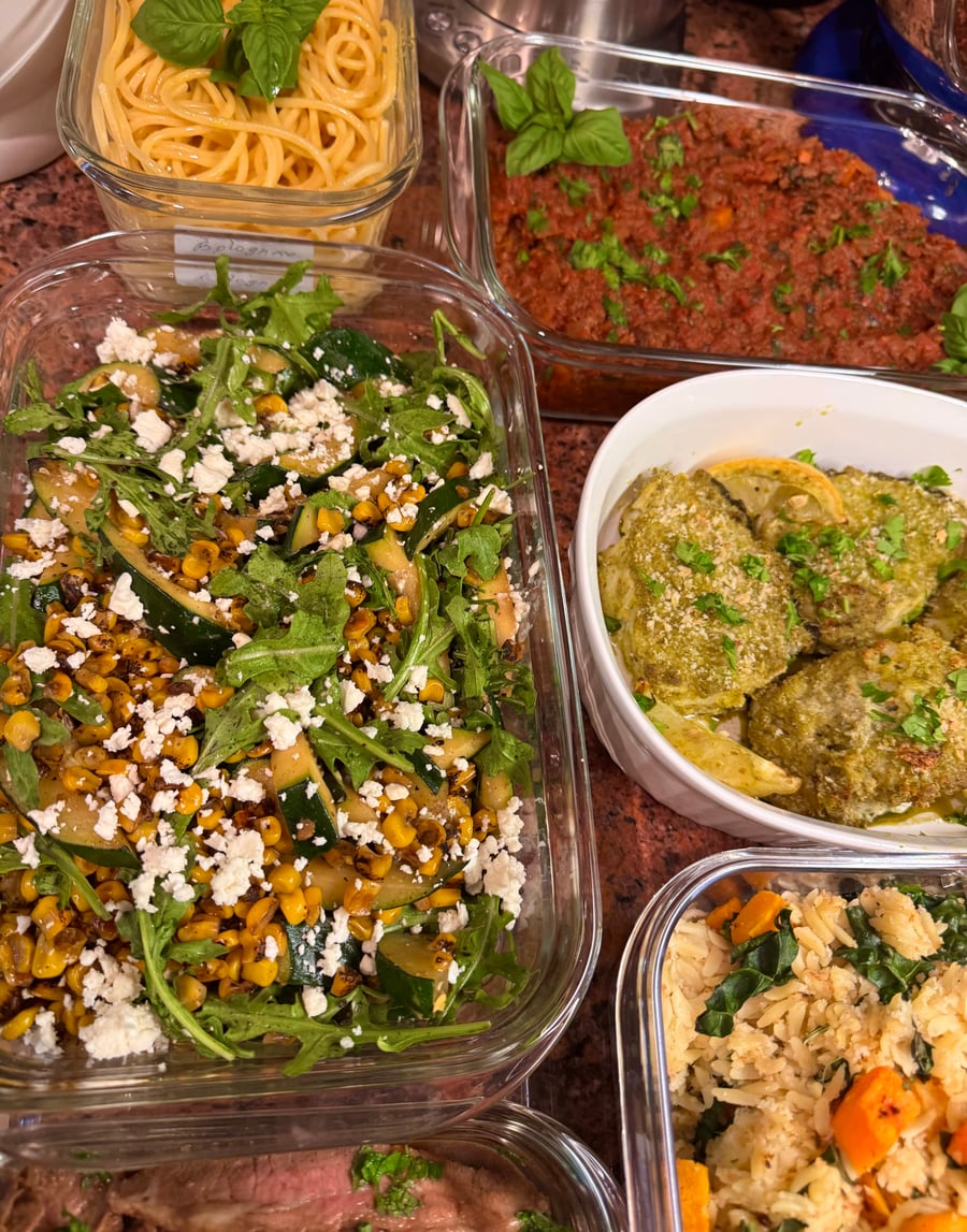 Glass meal prep containers filled with spaghetti, bolognese sauce, roasted zucchini corn salad with feta, herb-crusted chicken thighs, and a vegetable rice pilaf.