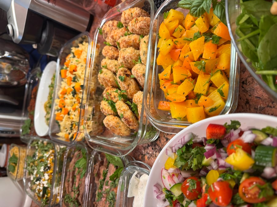 A variety of glass containers holding herb-crusted croquettes, golden roasted beets, fresh vegetable salad, and sliced seared protein garnished with fresh herbs.